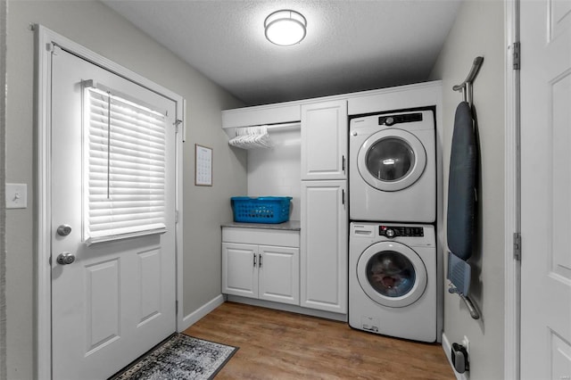 clothes washing area with light hardwood / wood-style flooring, stacked washer and clothes dryer, a textured ceiling, and cabinets