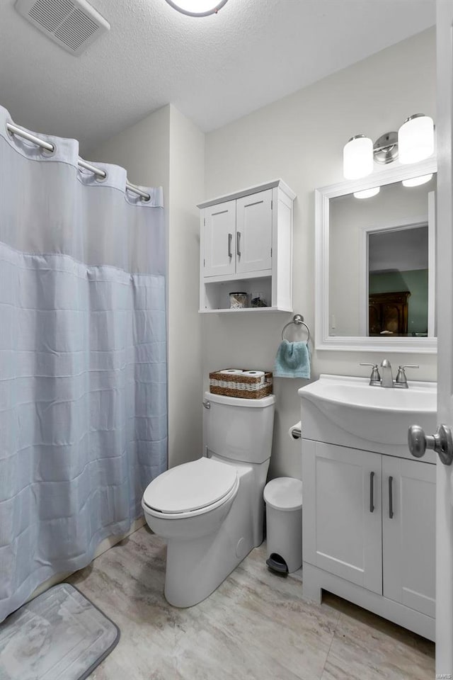 bathroom with a textured ceiling, toilet, a shower with shower curtain, and vanity