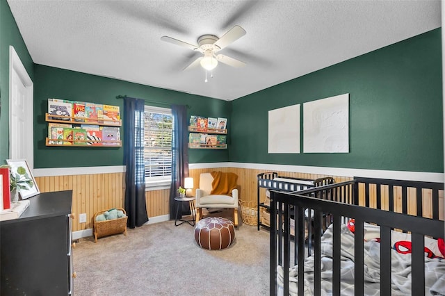 carpeted bedroom featuring a textured ceiling, ceiling fan, and a nursery area