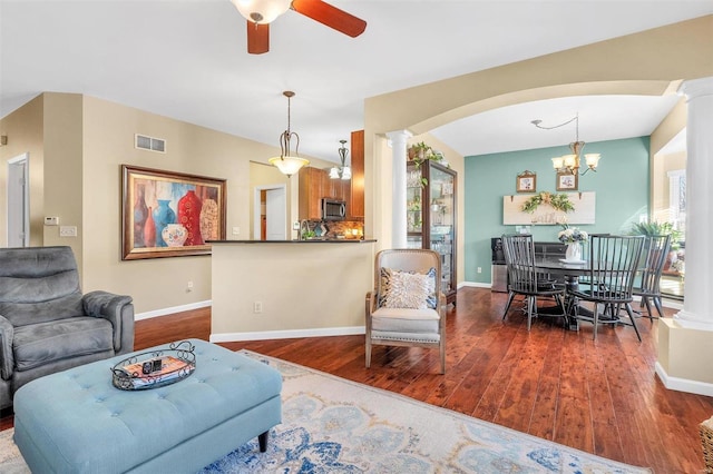 living room with ceiling fan with notable chandelier, dark hardwood / wood-style floors, and ornate columns