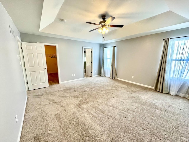 unfurnished bedroom featuring a spacious closet, ceiling fan, a tray ceiling, a closet, and light colored carpet