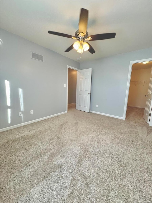 unfurnished bedroom featuring ceiling fan, a closet, a walk in closet, and carpet flooring