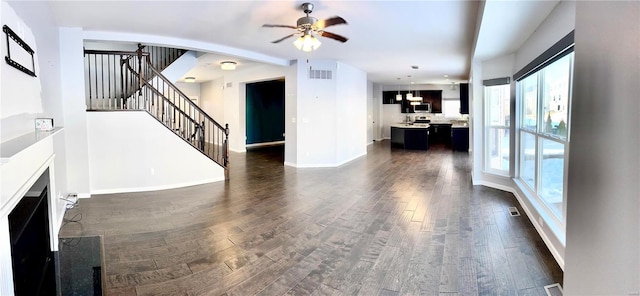 unfurnished living room featuring dark wood-type flooring, ceiling fan, and a healthy amount of sunlight