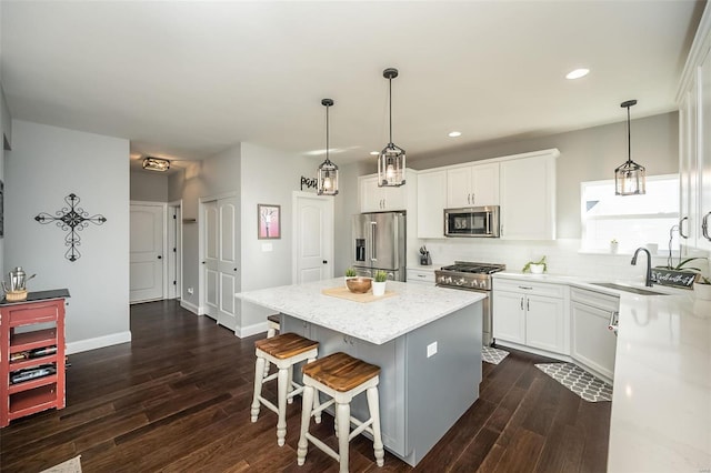 kitchen with appliances with stainless steel finishes, decorative light fixtures, white cabinetry, sink, and a center island