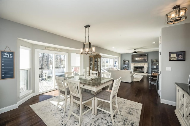 dining room with dark hardwood / wood-style flooring, ceiling fan with notable chandelier, and a fireplace