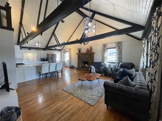 living room featuring wood-type flooring, sink, beamed ceiling, a stone fireplace, and high vaulted ceiling