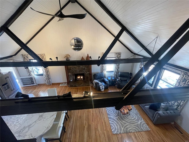 living room with ceiling fan, hardwood / wood-style floors, a stone fireplace, and lofted ceiling with beams