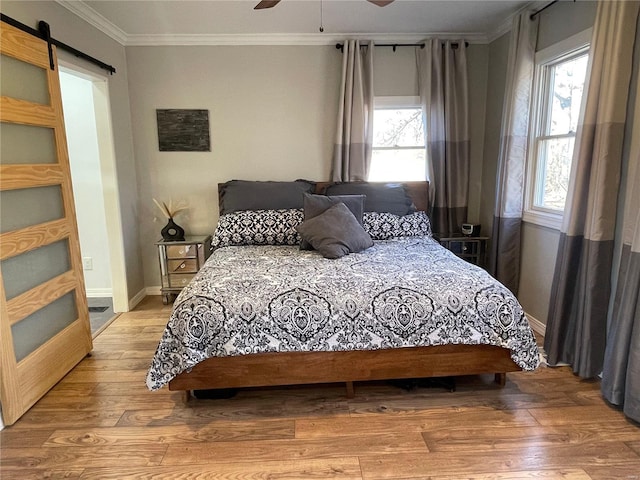 bedroom featuring ceiling fan, multiple windows, a barn door, and light wood-type flooring