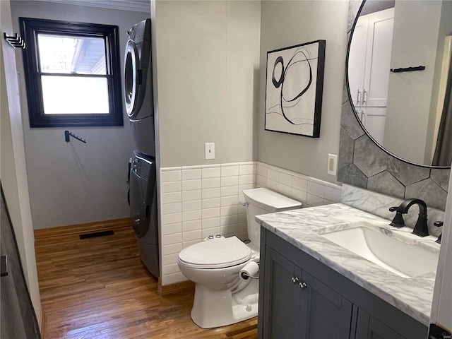 bathroom with toilet, vanity, tile walls, hardwood / wood-style floors, and stacked washer and dryer