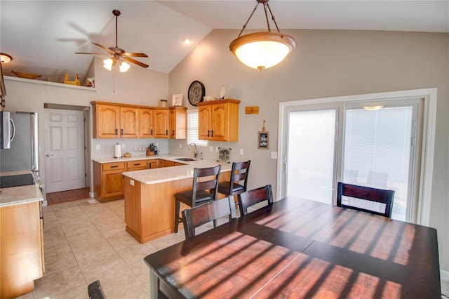 kitchen with a kitchen bar, stainless steel fridge, high vaulted ceiling, pendant lighting, and sink