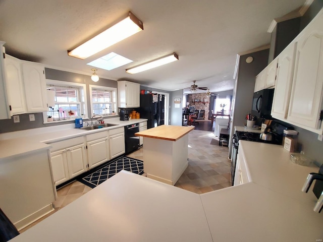 kitchen featuring white cabinets, black appliances, wood counters, a kitchen island, and sink