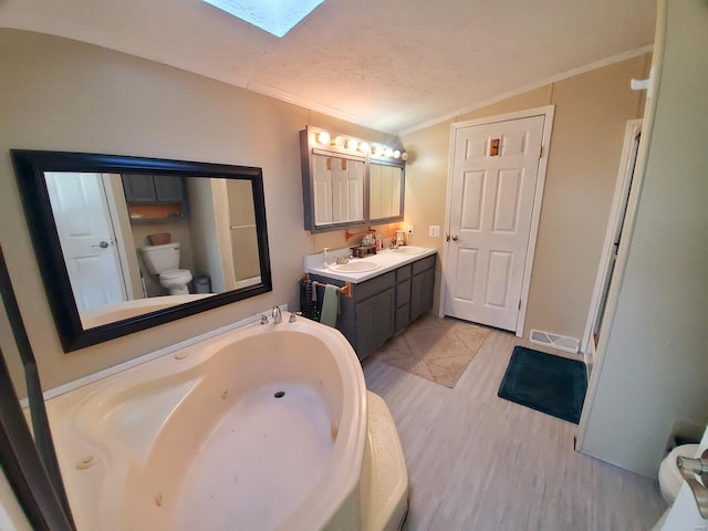 bathroom with vaulted ceiling with skylight, a textured ceiling, vanity, toilet, and a tub to relax in