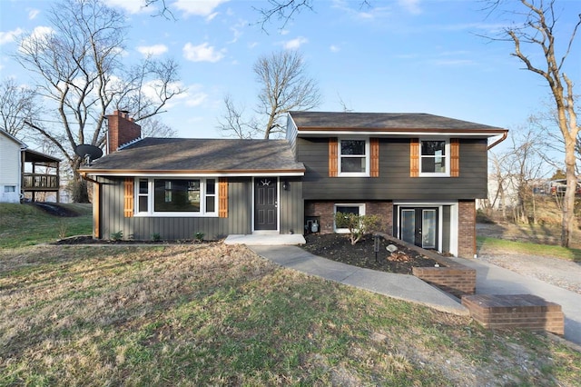 tri-level home with brick siding, board and batten siding, a front lawn, french doors, and a chimney