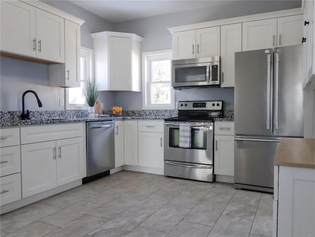 kitchen featuring sink, white cabinets, stainless steel appliances, and dark stone countertops