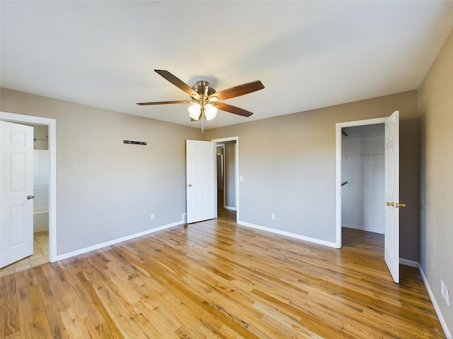 unfurnished bedroom featuring a spacious closet, a closet, ceiling fan, and light wood-type flooring