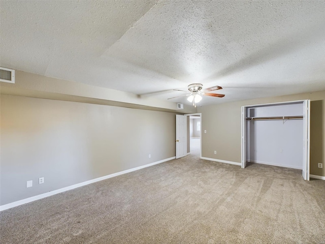 unfurnished bedroom with a closet, ceiling fan, light colored carpet, and a textured ceiling