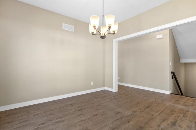 empty room with dark wood-type flooring and a notable chandelier