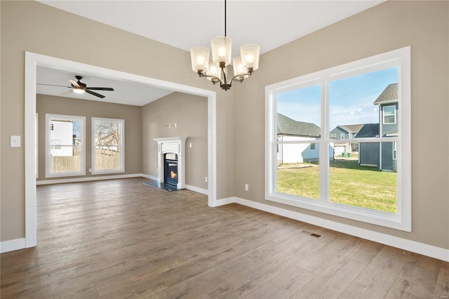 unfurnished living room featuring wood-type flooring, a wealth of natural light, and ceiling fan with notable chandelier