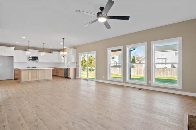 unfurnished living room featuring ceiling fan with notable chandelier and light wood-type flooring