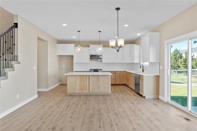 kitchen featuring white cabinets, appliances with stainless steel finishes, a center island, light hardwood / wood-style floors, and hanging light fixtures