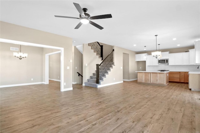 unfurnished living room with ceiling fan with notable chandelier and light hardwood / wood-style floors