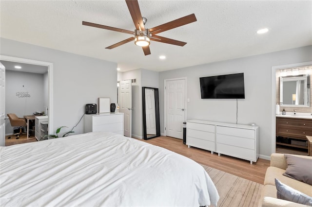 bedroom with ceiling fan, light hardwood / wood-style floors, a textured ceiling, and ensuite bath