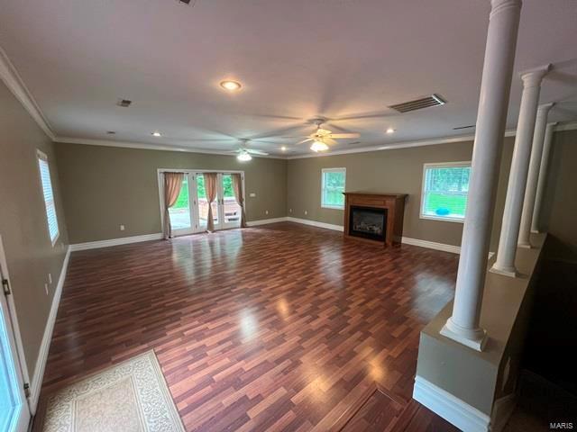 unfurnished living room featuring decorative columns, ornamental molding, dark wood-type flooring, and ceiling fan