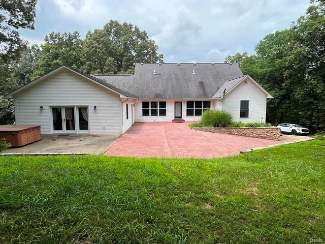 back of property featuring a hot tub, a patio, and a yard