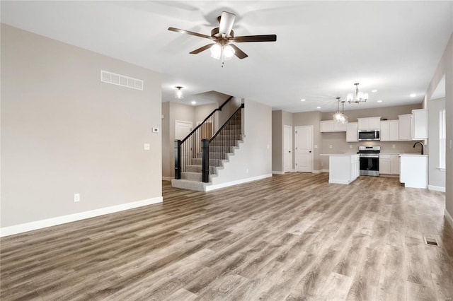 unfurnished living room with ceiling fan with notable chandelier, light hardwood / wood-style flooring, and sink