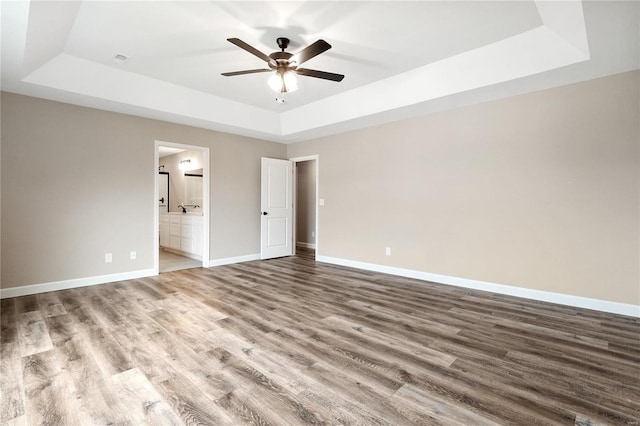 unfurnished bedroom featuring ensuite bath, ceiling fan, a tray ceiling, and hardwood / wood-style flooring