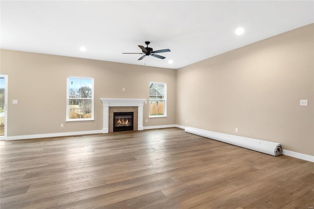 unfurnished living room with ceiling fan, hardwood / wood-style floors, a tile fireplace, and a healthy amount of sunlight