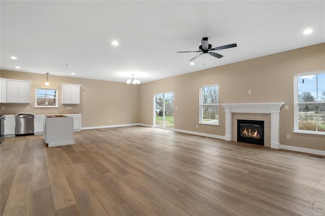 unfurnished living room featuring ceiling fan with notable chandelier, light hardwood / wood-style floors, and a tiled fireplace