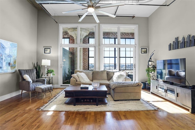 living room with ceiling fan, wood-type flooring, and a towering ceiling