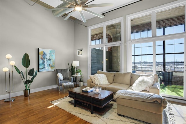 living room with ceiling fan, a high ceiling, wood-type flooring, and a healthy amount of sunlight