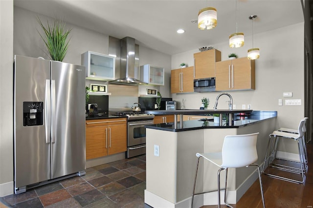 kitchen with kitchen peninsula, appliances with stainless steel finishes, range hood, pendant lighting, and a breakfast bar