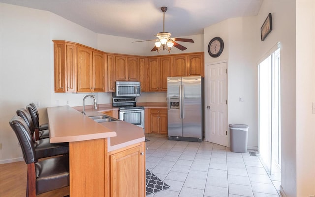 kitchen featuring kitchen peninsula, appliances with stainless steel finishes, sink, light tile patterned floors, and a kitchen bar