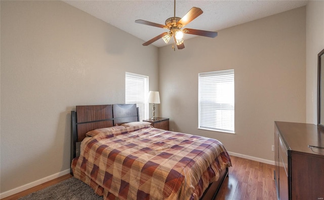 bedroom featuring ceiling fan, multiple windows, lofted ceiling, and hardwood / wood-style floors