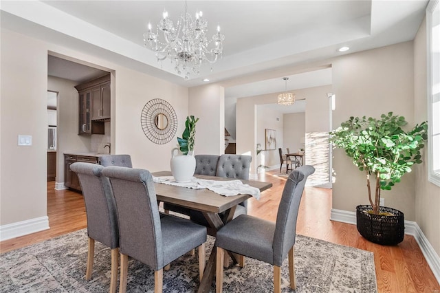 dining area featuring a tray ceiling, light hardwood / wood-style flooring, and an inviting chandelier