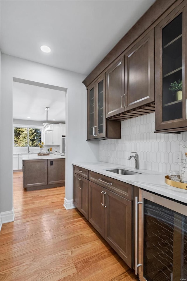 bar with light wood-type flooring, dark brown cabinets, beverage cooler, pendant lighting, and sink