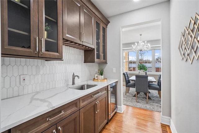 kitchen featuring wine cooler, a notable chandelier, sink, light hardwood / wood-style flooring, and light stone counters