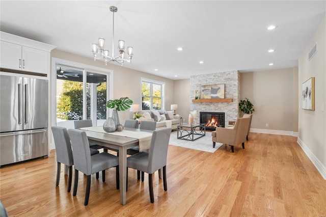 dining area featuring ceiling fan with notable chandelier, a stone fireplace, and light hardwood / wood-style flooring