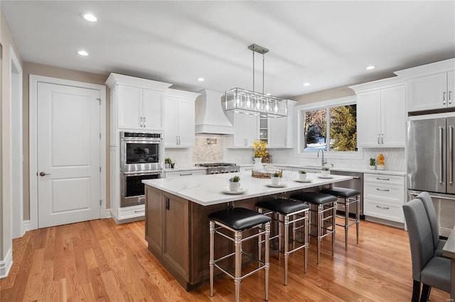 kitchen with white cabinets, appliances with stainless steel finishes, custom range hood, and a kitchen island