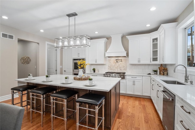 kitchen featuring appliances with stainless steel finishes, a kitchen island, custom exhaust hood, sink, and a breakfast bar area