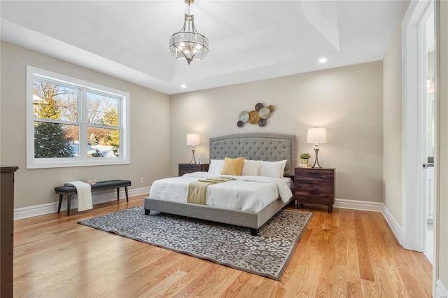 bedroom featuring a tray ceiling, light wood-type flooring, and an inviting chandelier