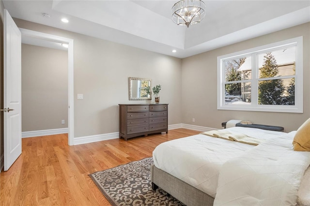 bedroom featuring a tray ceiling, light hardwood / wood-style flooring, and a notable chandelier