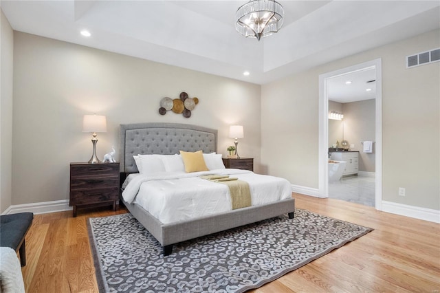 bedroom with hardwood / wood-style flooring, ensuite bath, and a chandelier