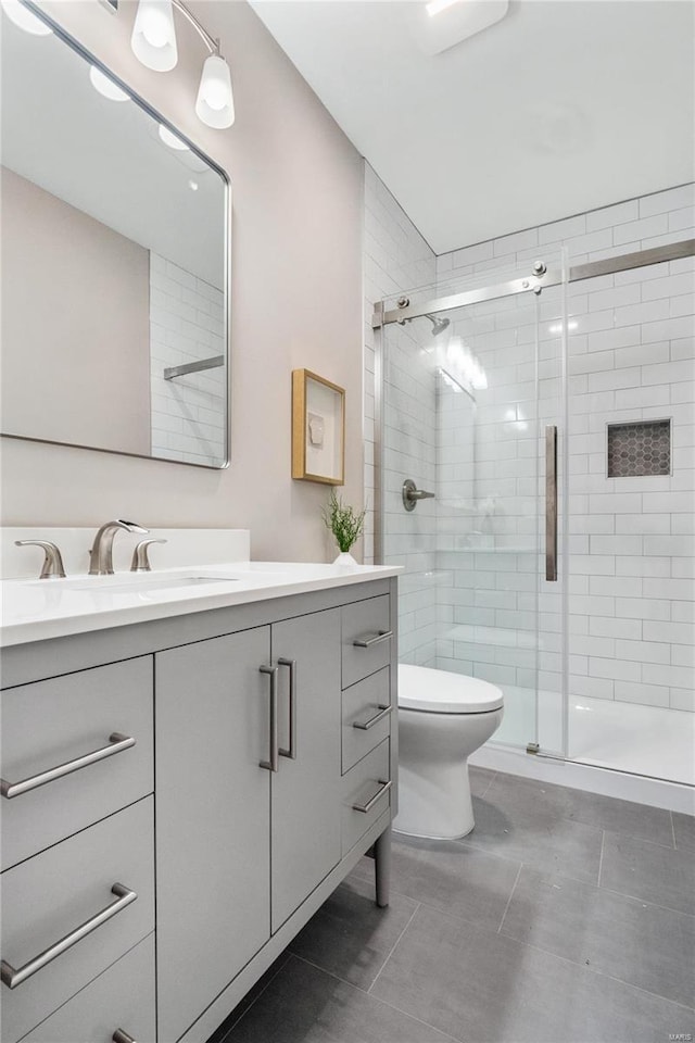 bathroom with toilet, vanity, tile patterned flooring, and a shower with shower door