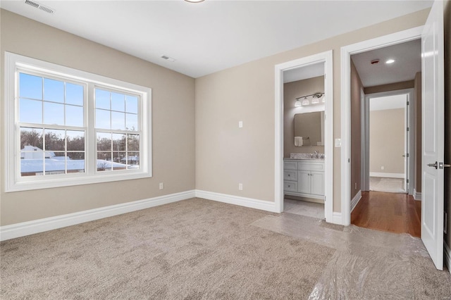 unfurnished bedroom featuring ensuite bath, light carpet, and sink