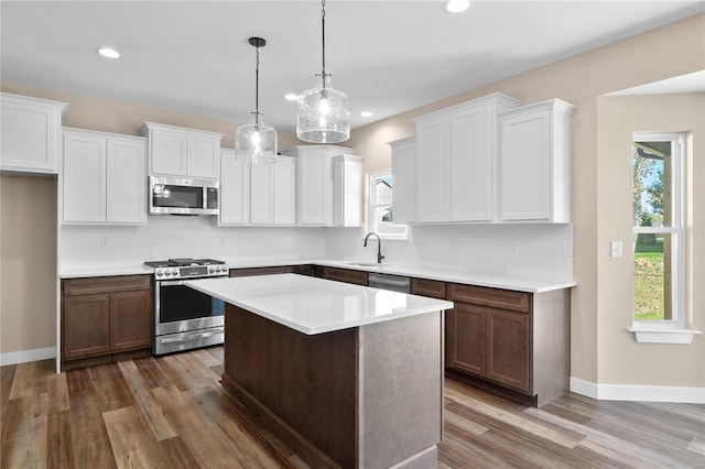 kitchen with a kitchen island, white cabinetry, stainless steel appliances, hanging light fixtures, and dark hardwood / wood-style floors