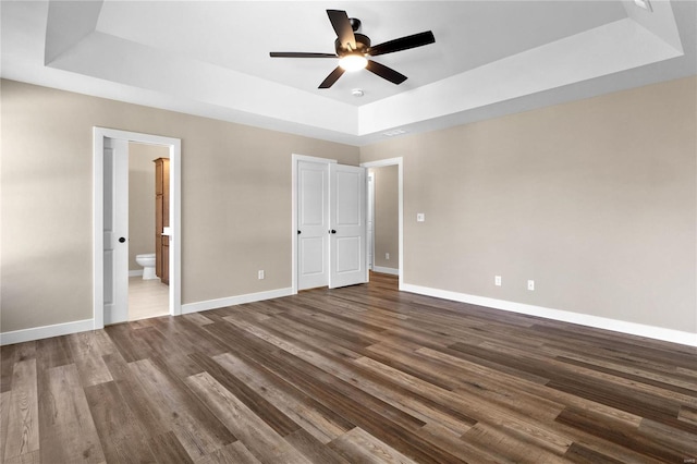 unfurnished bedroom with ceiling fan, ensuite bath, and a raised ceiling